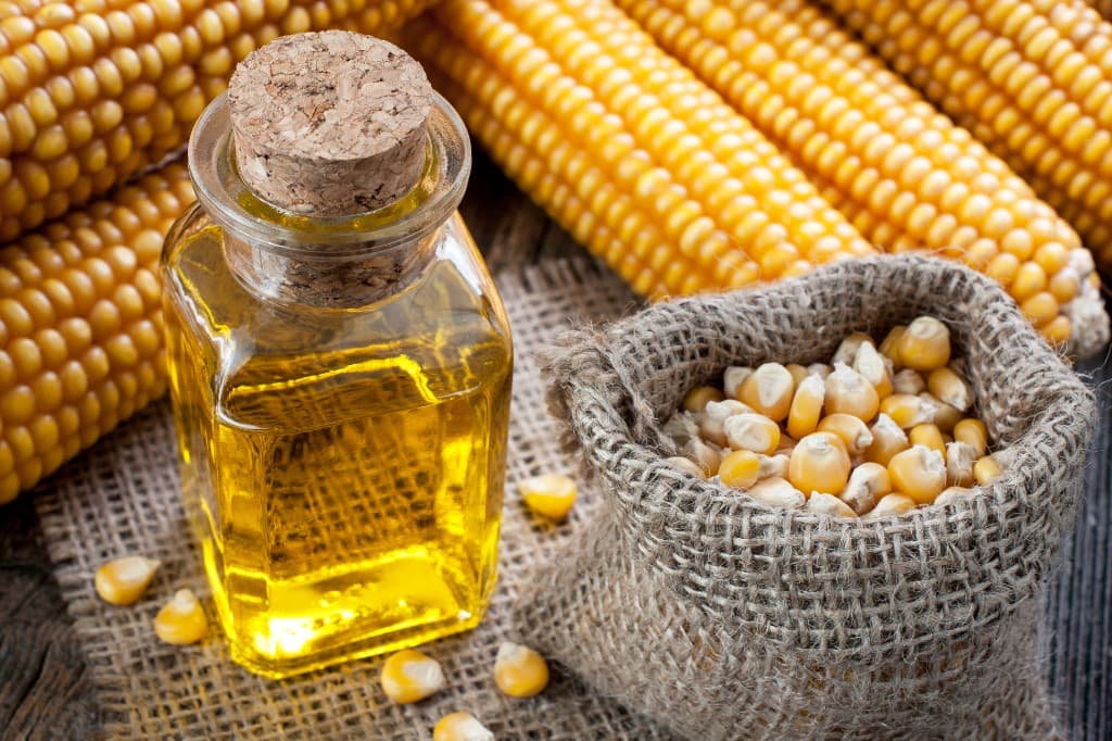 Bottle of golden popcorn oil with corn kernels for popcorn machine rental add-ons in South Florida.