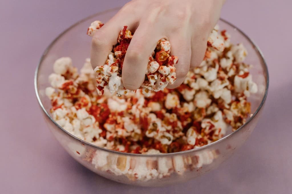 Hand picking up seasoned popcorn from a bowl for a popcorn machine rental add-on in South Florida.